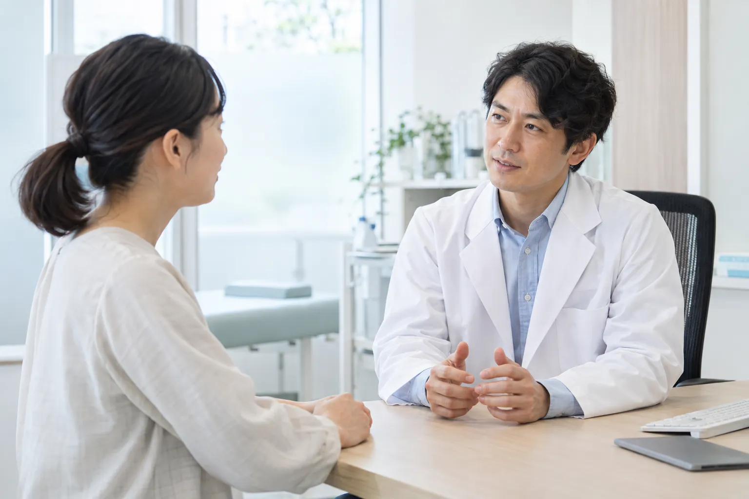 診察机を挟んで女性患者と話す男性医師のイメージ